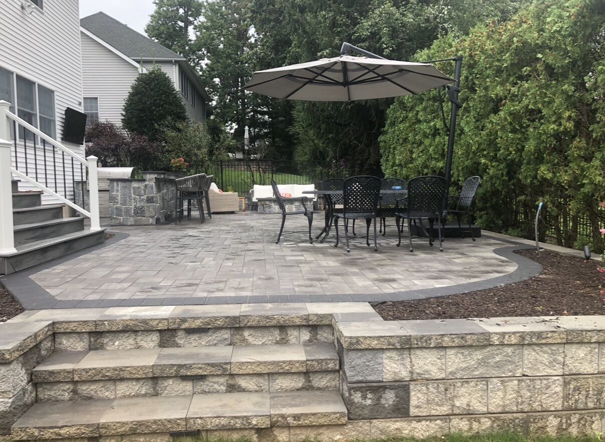 Finished paver patio with dining set, umbrella, and retaining wall steps