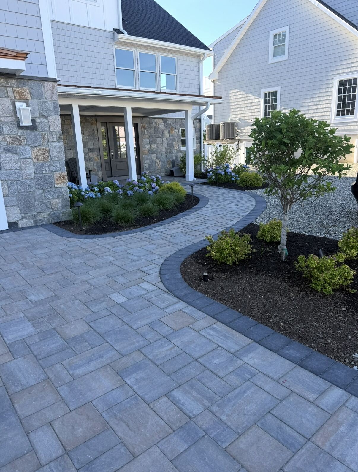 Curved paver walkway leading to a stone-veneer home entrance